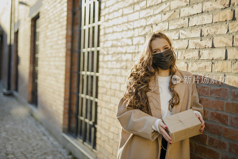 年轻女子戴着黑色防护面罩，手持礼盒