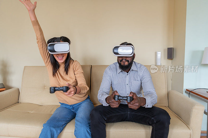 兴奋的多民族年轻夫妇正在用VR眼镜和手柄玩视频游戏，度过美好的时光。