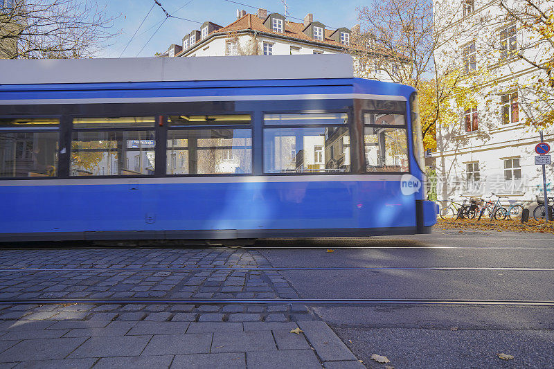 模糊的蓝白有轨电车在一个城市设置与汽车，树木和秋叶