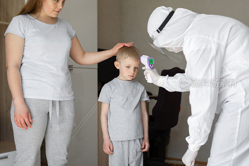 儿科医生或医生用红外线额头温度计枪检查小学男孩的体温，以了解病毒症状——冠状病毒疫情爆发的概念。