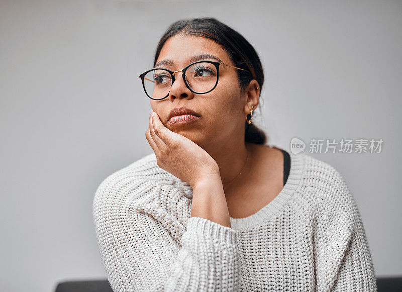 这张照片拍摄的是一个年轻女子坐在家里的沙发上，看起来若有所思