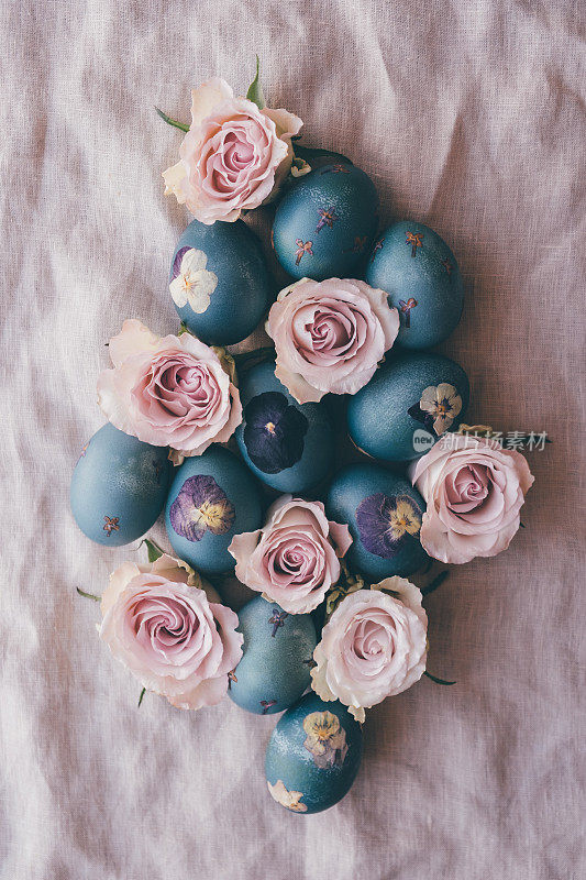 自然染色的青蓝压花复活节蛋在中性米色桌布背景玫瑰花盛开，俯视图。手工工艺，天然装饰。