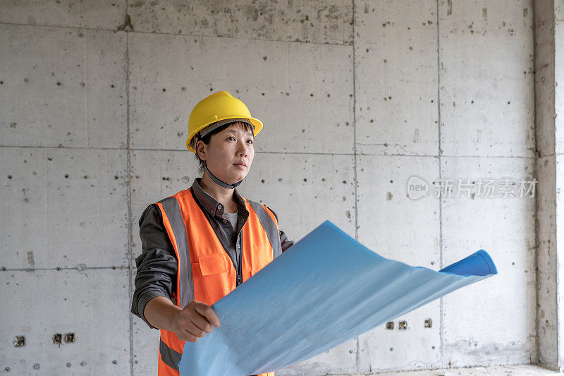 在施工现场，一位亚洲女工程师拿着设计图，正在检查建筑资料