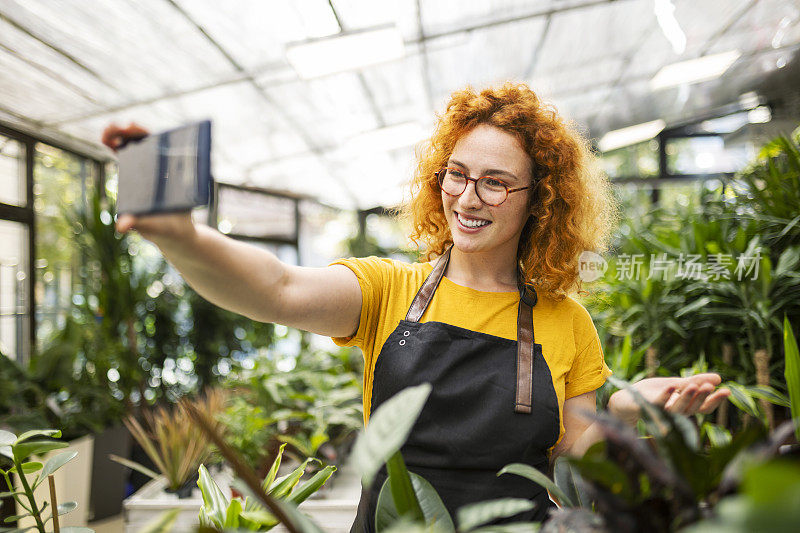 年轻的红发女子在花店工作，与盆栽植物自拍