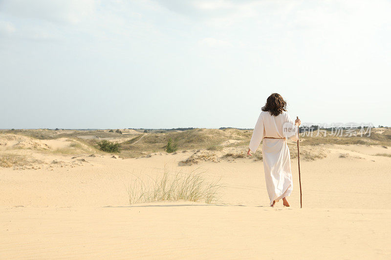 耶稣基督拄着拐杖走在沙漠里，背影。空间的文本