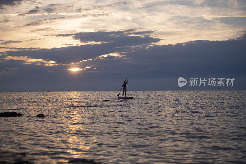 黄昏时分，妇女站起来划桨冲浪