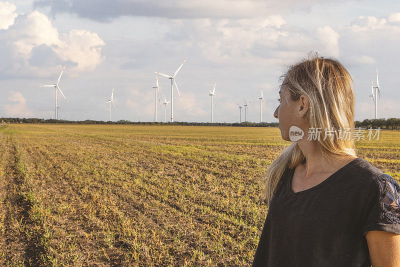 田里的女农民望向远方，风力涡轮机在远处