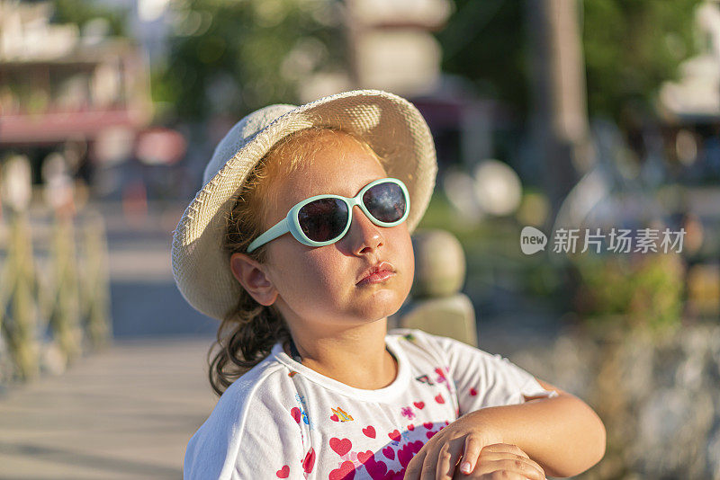 一个戴着帽子和太阳镜的女孩在海滩上的肖像
