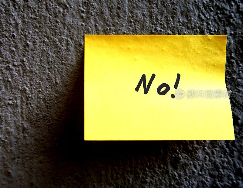 灰色粗糙的水泥墙上有一个黄色的便签本，上面写着“NO!”拒绝的概念