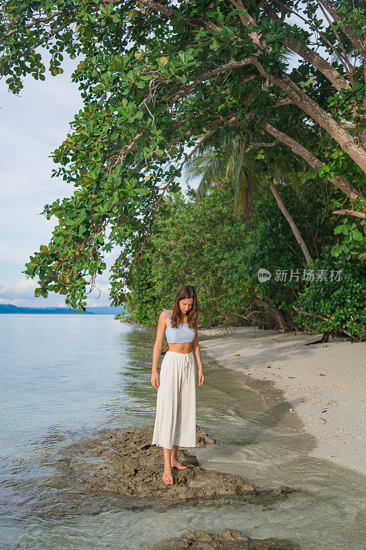 年轻女子走在树下的白色沙滩上