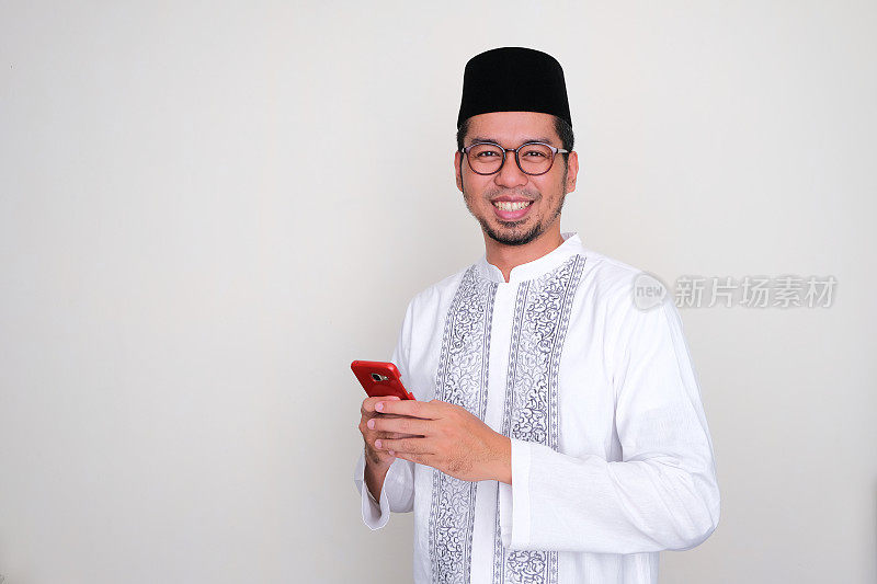 穆斯林亚洲男子拿着手机对着镜头微笑