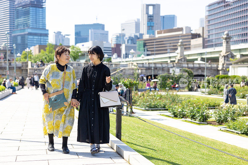 年轻女子和她的祖母一起走在城市的公园里