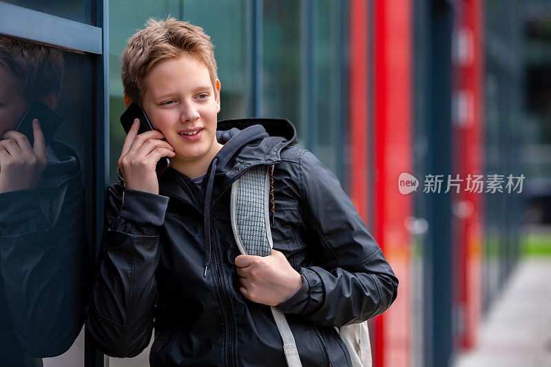 十几岁的男孩微笑着用手机和朋友聊天
