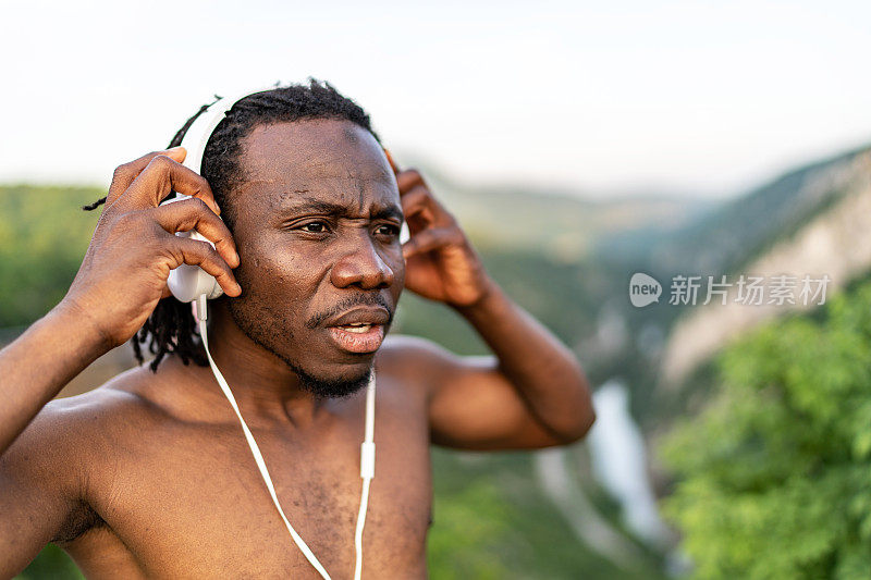 一个赤膊的年轻非洲运动员站在大自然中听音乐的肖像