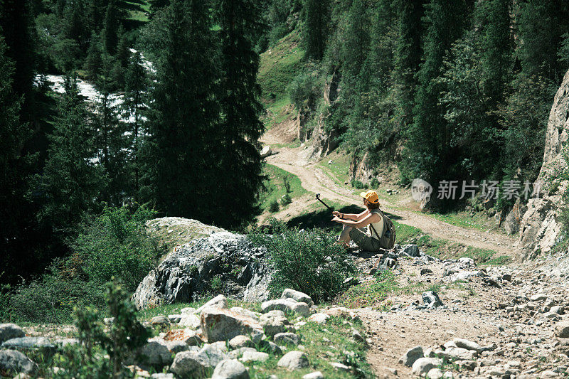 女游客在南天山狭窄峡谷的山河上方的岩石上拍摄视频