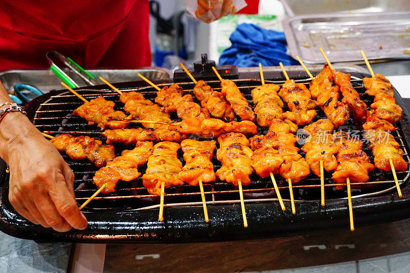 用竹签在电炉上烤鸡，卖家的手在烤架上烤鸡。烤鸡烧烤特写。美味的亚洲料理。马来西亚沙爹鸡。