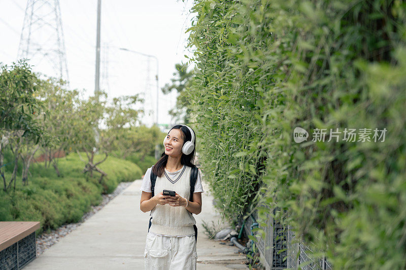 微笑的女人用智能手机和耳机拥抱大自然的旋律