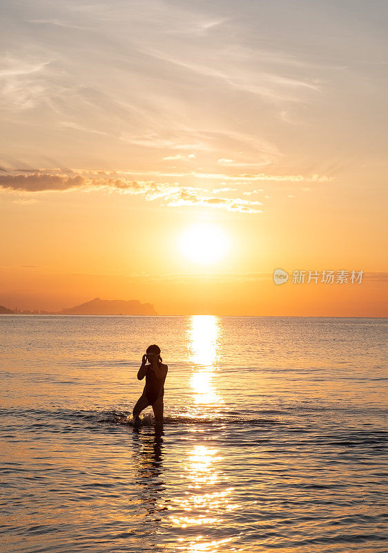 夏天，一个小女孩在海里游泳，看着海面上的日出。阿利坎特圣胡安海滩