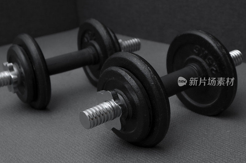 健身背景。两个10公斤重的哑铃放在灰色垫子上。运动概念:灰色垫子，两个10公斤重的黑色哑铃