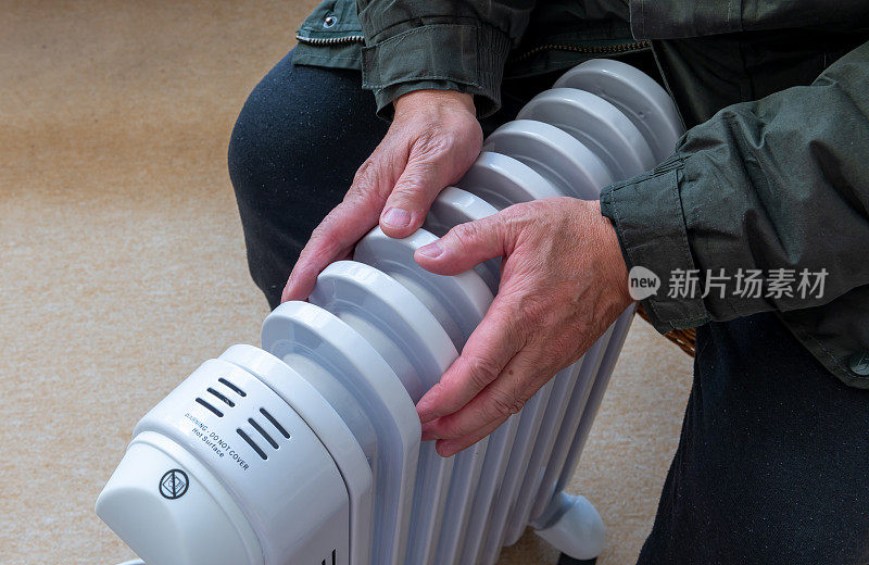 一个人坐在房间里抱着便携式电暖器，试图在冬天的寒冷中保持温暖。