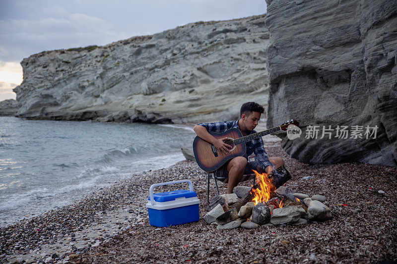 一个年轻人在沙滩上篝火旁弹吉他。