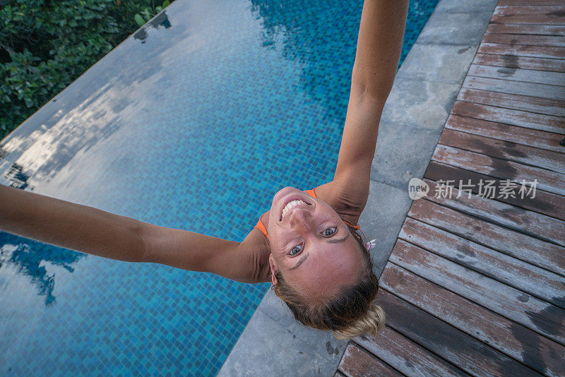 女人在泳池边自拍，而享受热带度假在巴厘岛-人们旅行乐趣分享记忆的概念