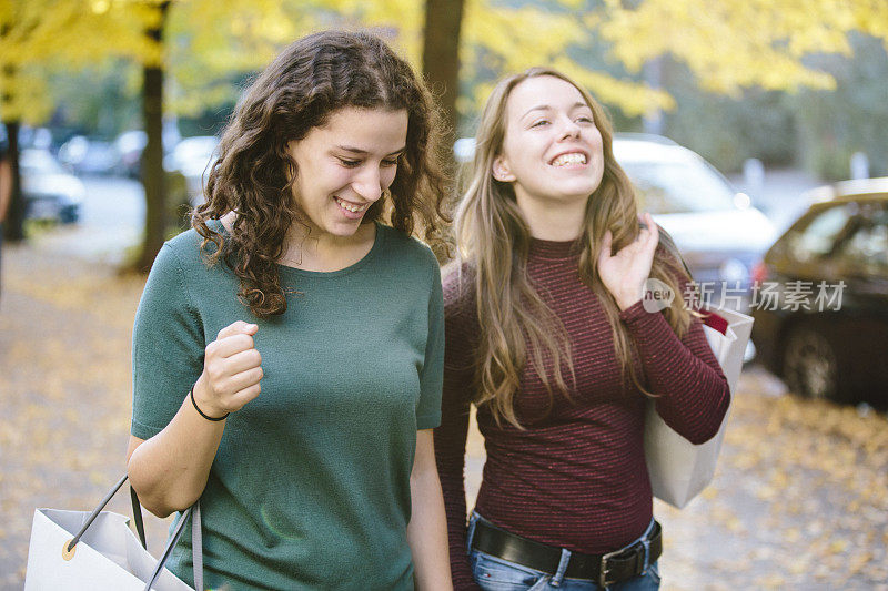 购物:两个年轻的女人拿着购物袋走在街上