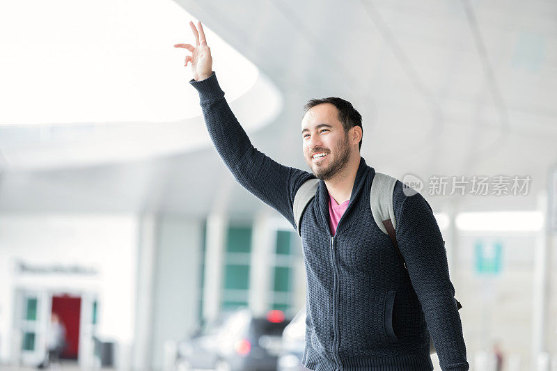 年轻的商务旅行者在机场候机楼外挥手叫出租车或朋友