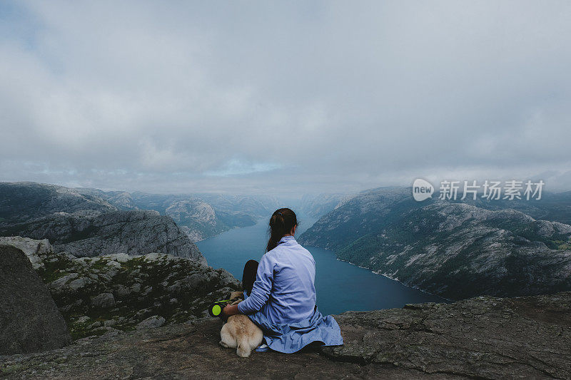 一个女人和一只狗在看挪威布道石上吕瑟峡湾的风景