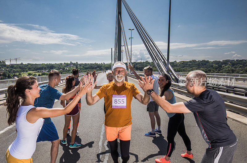 快乐的老年马拉松运动员在桥上和他的支持者打招呼。