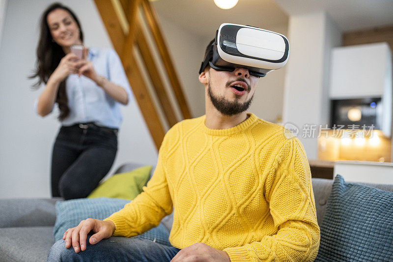 一名年轻人用虚拟现实头盔和女友用智能手机拍摄他的视频