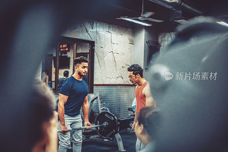健身教练在健身房帮助一个肌肉男举重