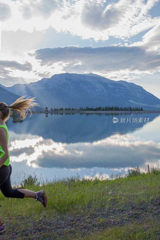 年轻的女子越野跑运动员沿着山中的湖岸蹦蹦跳跳