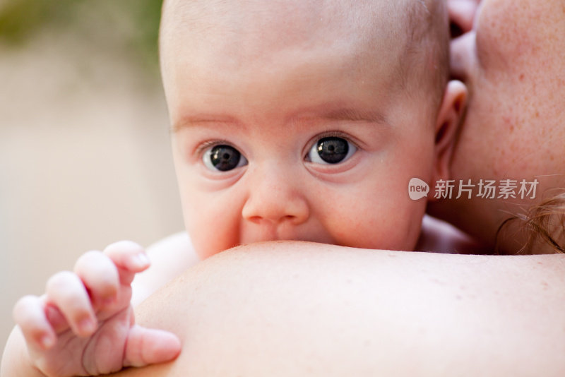 三个月大的婴儿从她妈妈的肩膀上盯着她