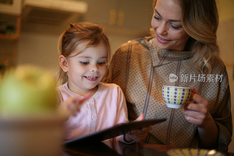 母亲和女儿在平板电脑上看书。