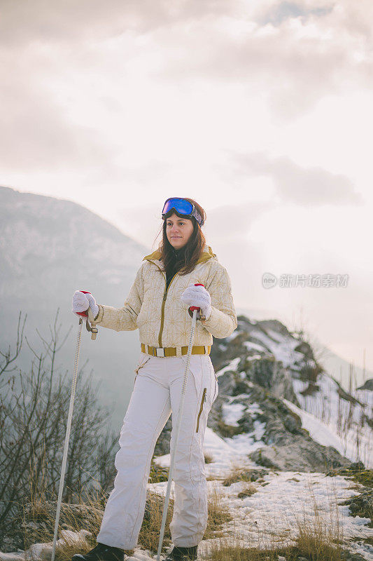 近景美丽的年轻女子在冬天的衣服站在一边，手拿木棍的背景雪山