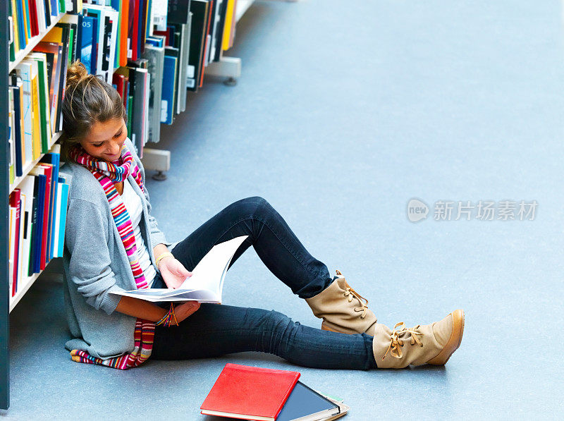 女学生坐在书架旁边的书在图书馆