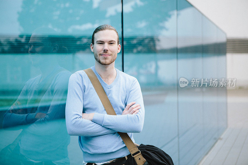 一名年轻白人男子倚靠在蓝色玻璃墙上的肖像