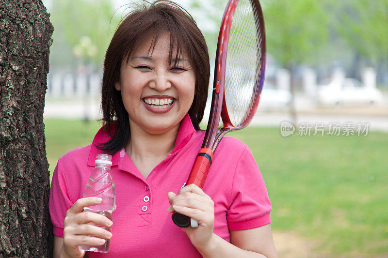 女人高兴地拿着矿泉水和网球拍