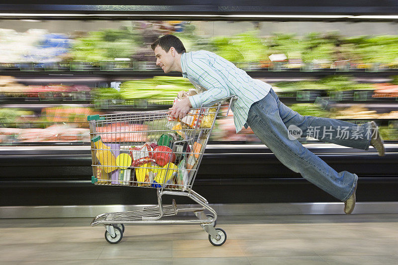 一名男子倚靠在超市手推车上，双腿悬在空中，动作模糊