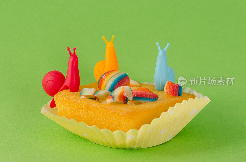 扁平纸杯蛋糕在绿色背景与彩色蜗牛和糖果