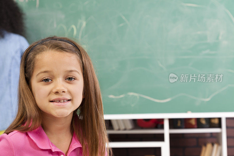 小学女孩在教室里伏案工作。黑板和学生背景。