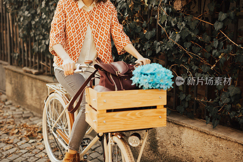 女孩骑着自行车，背着背包和蓝色的花在篮子里