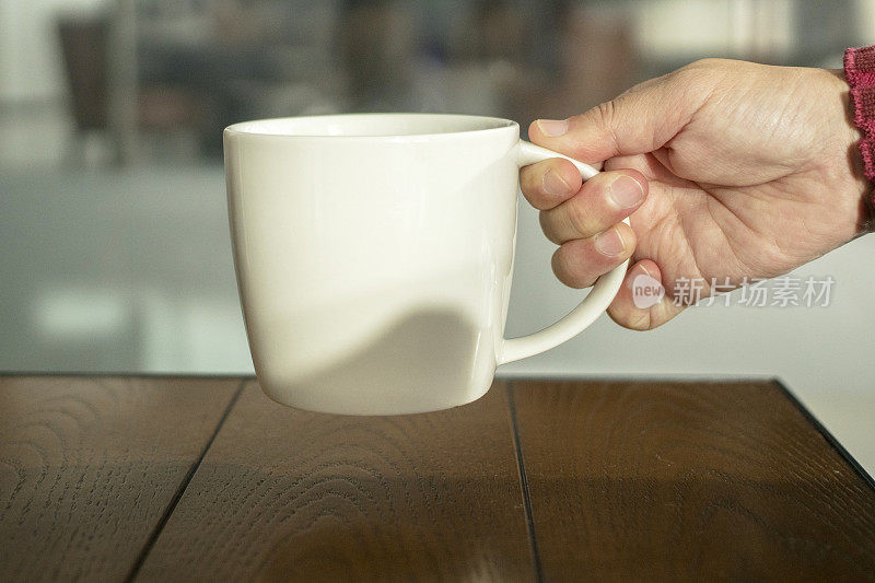 手里拿着一个咖啡杯，放在桌上