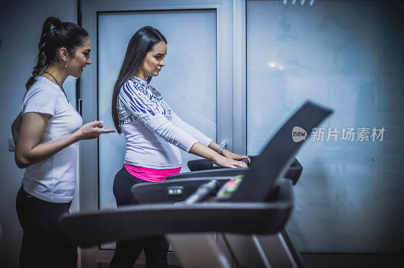 孕妇在健身教练的帮助下在健身房锻炼