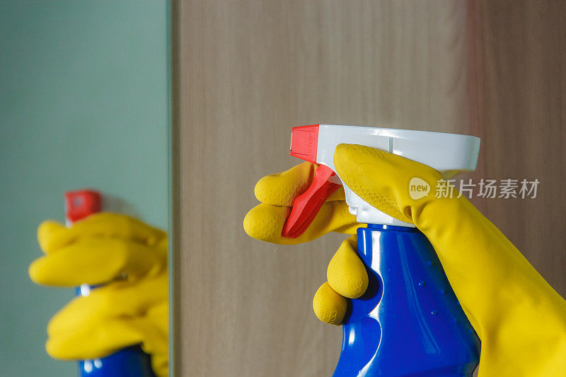 女性手戴黄手套用喷雾清洁剂清洁镜子。蓝瓶，家务，春季大扫除的概念。