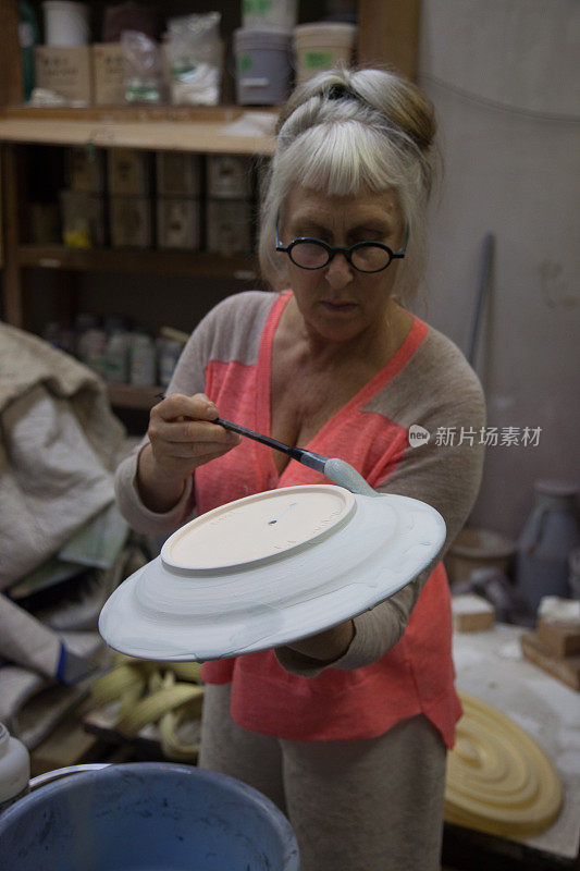 陶艺艺术家在准备烧制的陶瓷作品上釉，盘浸蓝釉后滴水，年长的白种女性，白发，彩发，驻日本茂木艺术家
