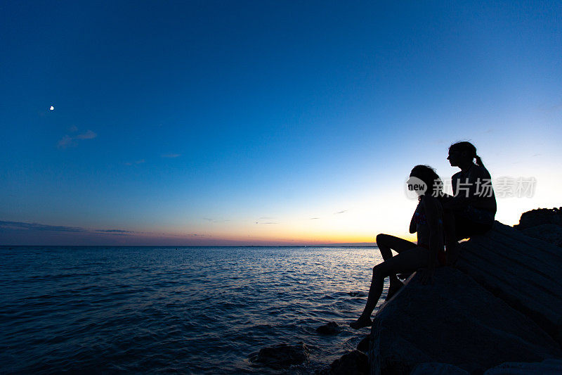 黄昏时分一对夫妇坐在海岸线上的剪影