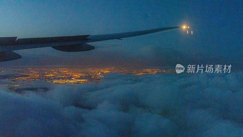 这架飞机的机翼在国际飞行中迎着天空和云层，鸟瞰着灯火通明的城市夜景。
