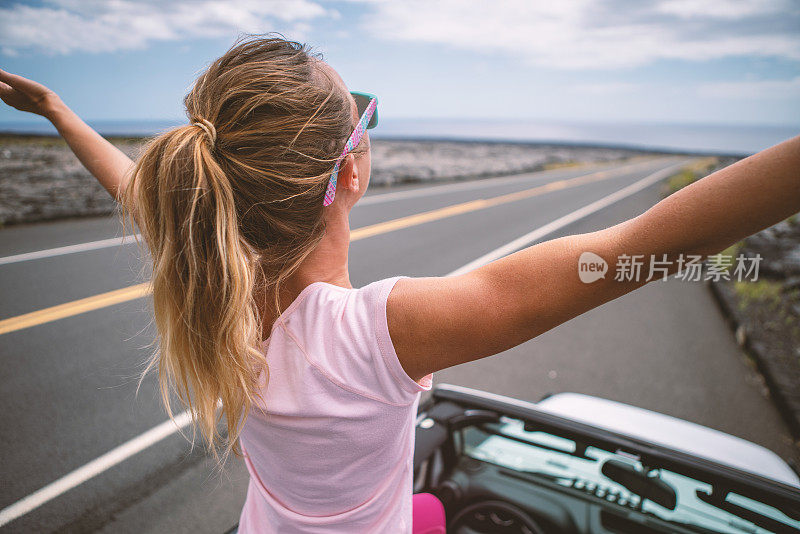 年轻女子坐在4x4汽车上，双臂伸开享受公路旅行